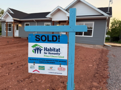 image of a newly built duplex, with a SOLD sign as the focus in front of the building. The sign includes the Habitat PEI logo as well as the logos of project sponsors and donors.